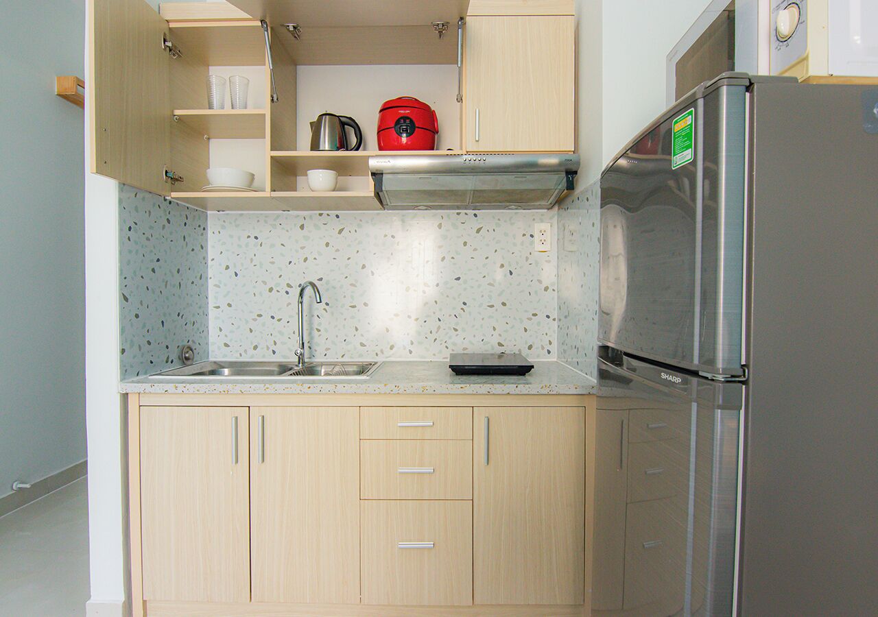 A kitchen with wooden cabinets, a stainless steel refrigerator, and a countertop with a kettle and cups.