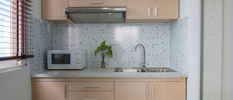 Una cocina con armarios de madera, microondas, fregadero y ventana con persianas.