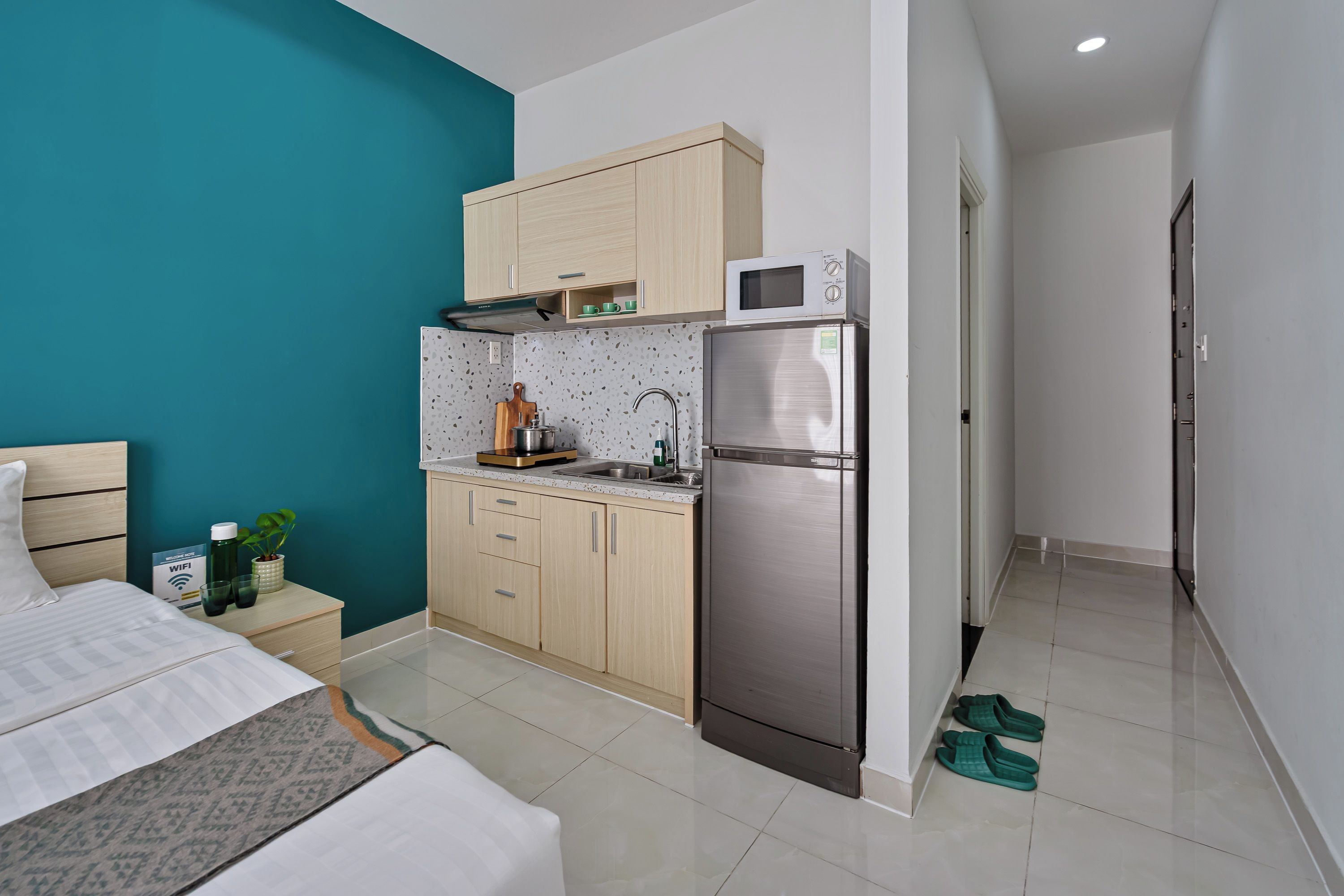 A compact hotel room with a bed, kitchenette, and a small bathroom.
