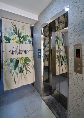 An elevator with a digital display, a welcome sign with floral patterns, and a sign indicating a free pantry. - Lumina Home (Ho Chi Minh City)