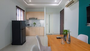 A modern kitchen with a refrigerator, microwave, and wooden cabinets. There is a dining table with chairs and a potted plant. - Lumina Home (Ho Chi Minh City)