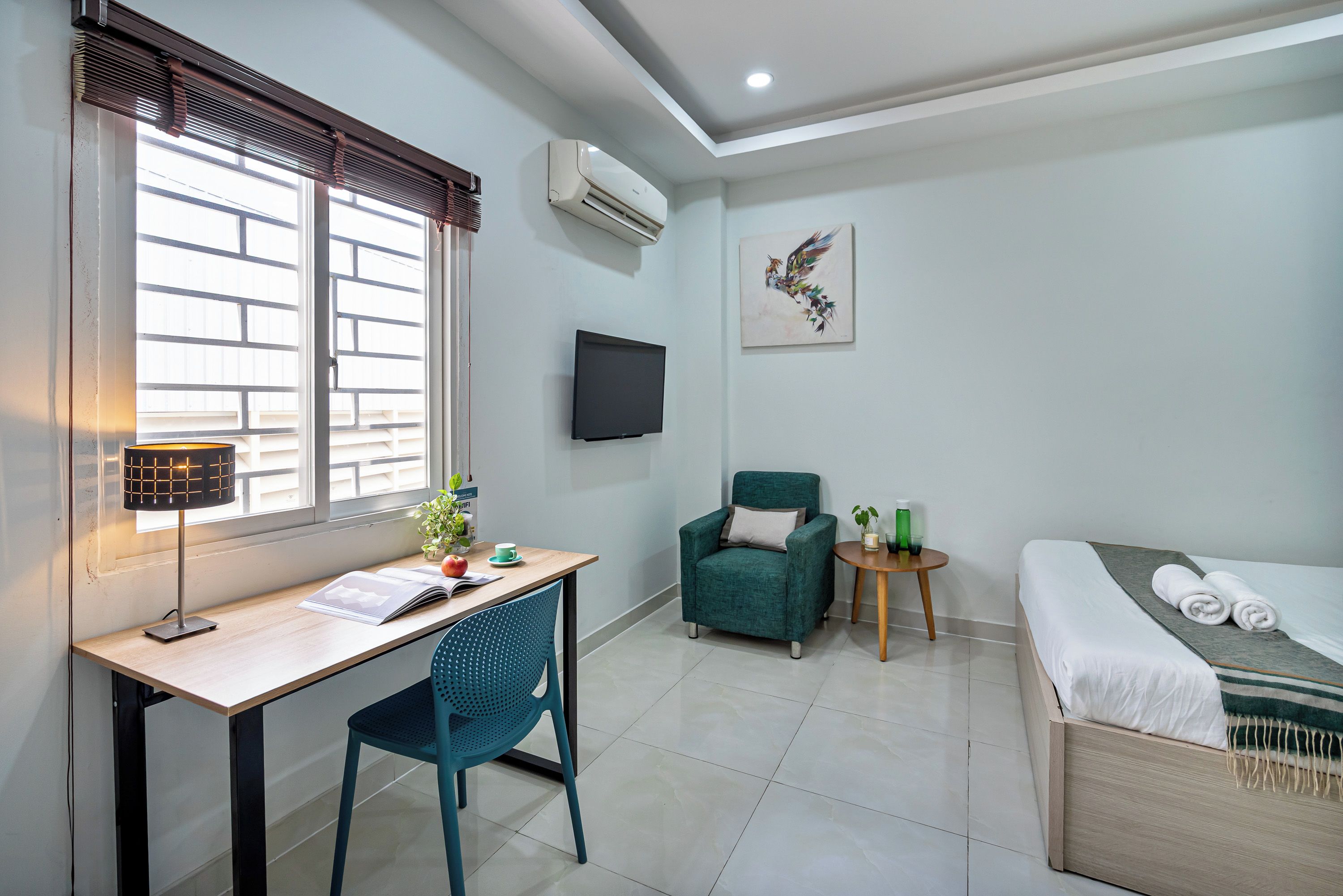 Une chambre d’hôtel équipée d’un bureau, d’une chaise, d’un lit et d’une petite table sur laquelle se trouve une plante.