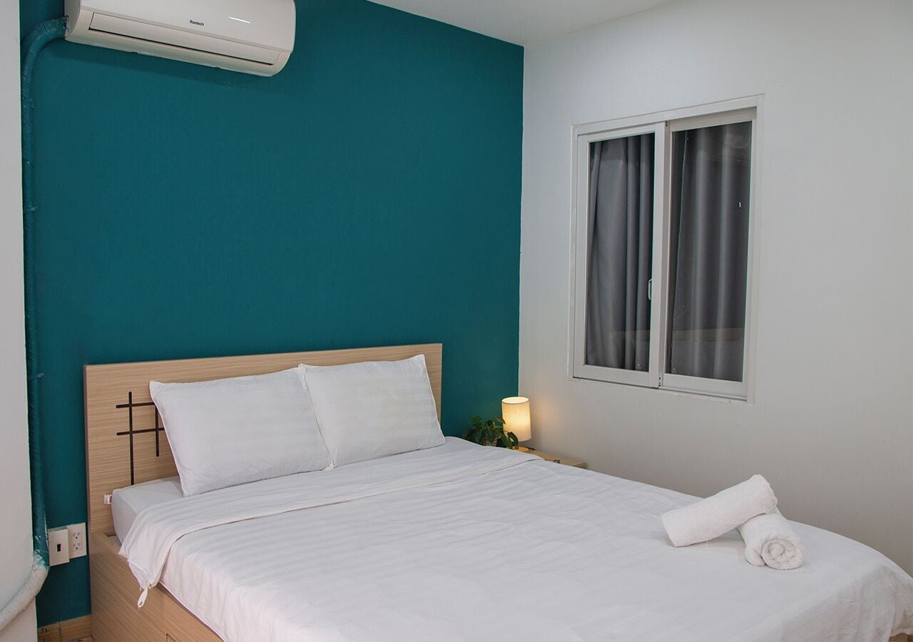 Una cama bien hecha con sábanas blancas, cabecera de madera y una pared de acento color turquesa.