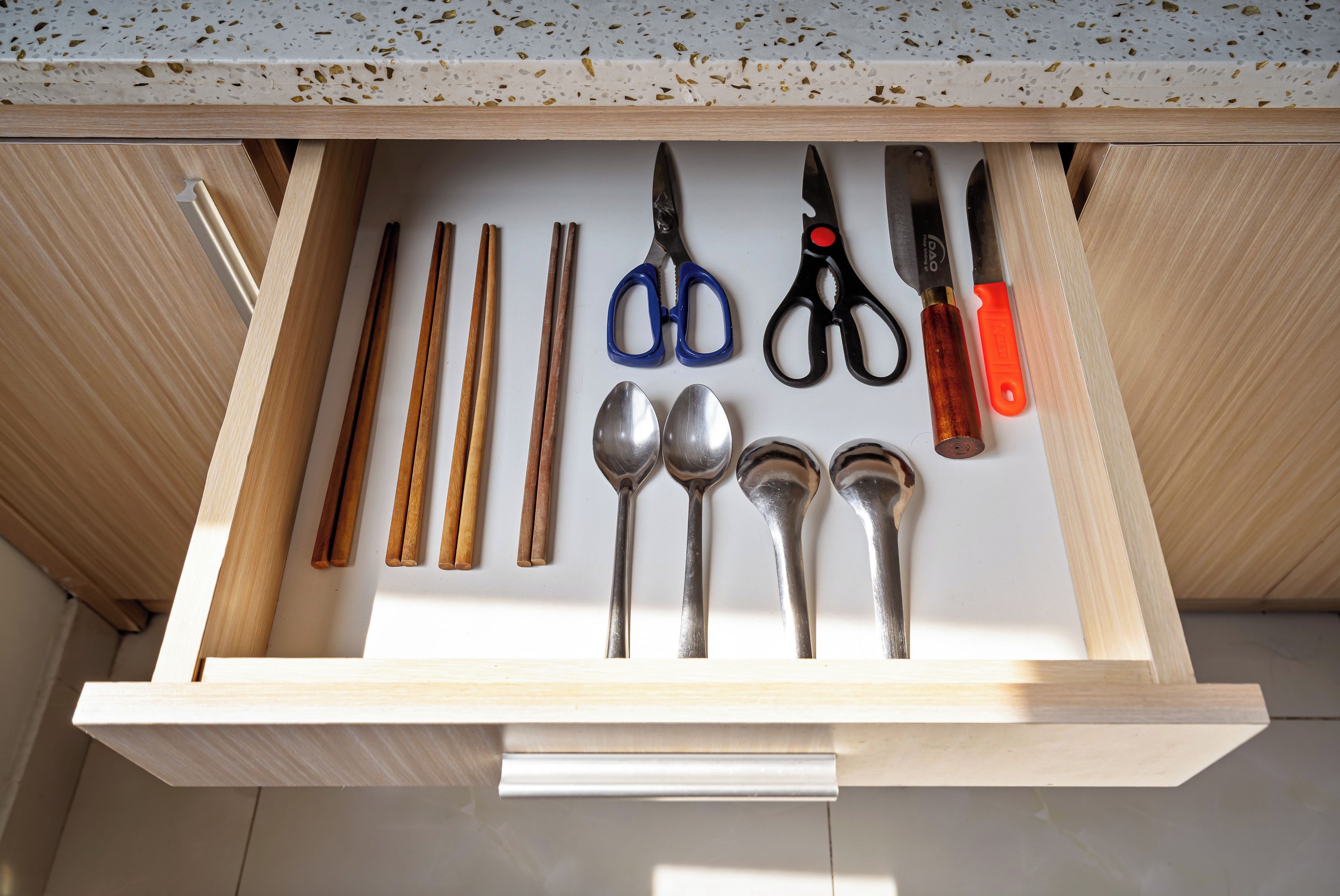 Un cajón con varios utensilios de cocina, incluyendo cucharas, un par de tijeras y palillos.