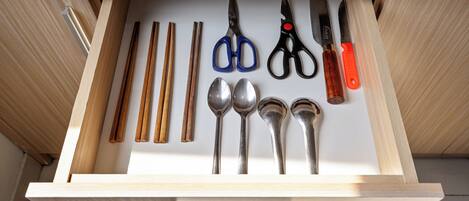 Un cajón con varios utensilios de cocina, incluyendo cucharas, un par de tijeras y palillos.