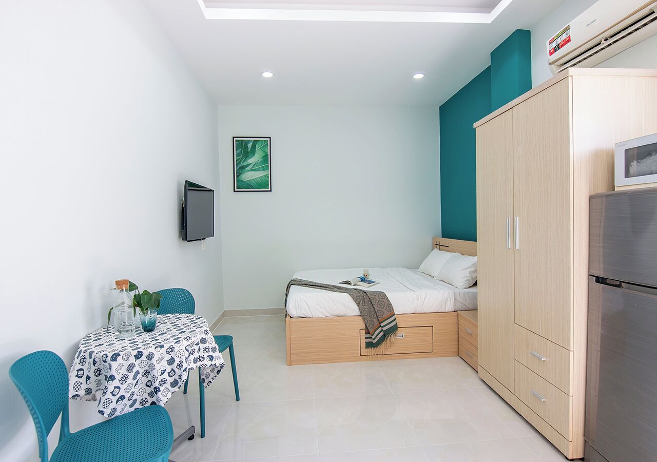 A compact room with a bed, a table with chairs, a wardrobe, and a built-in air conditioning unit.