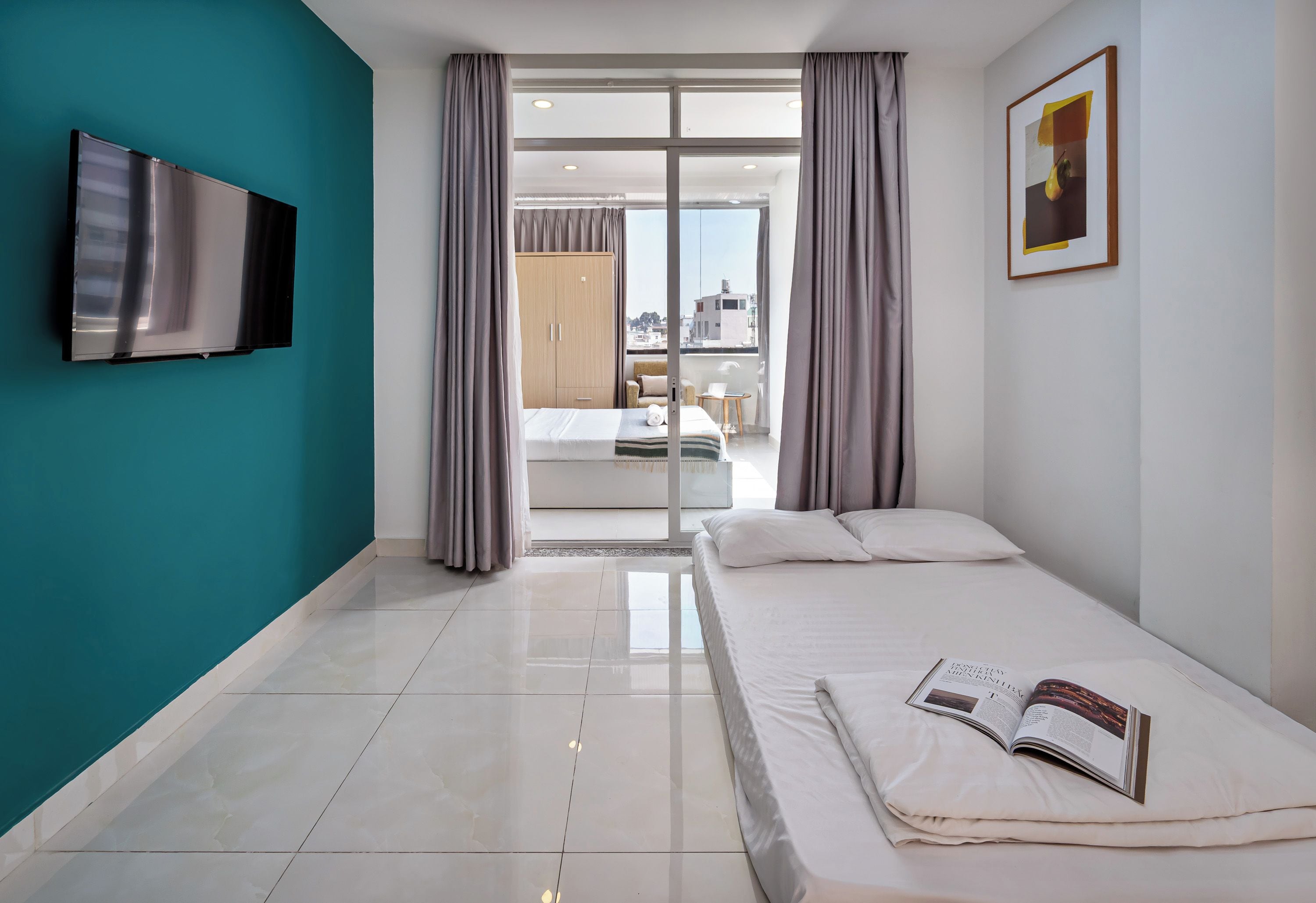 A modern hotel room with a large bed, a flat-screen TV, and a view of the city through the window.