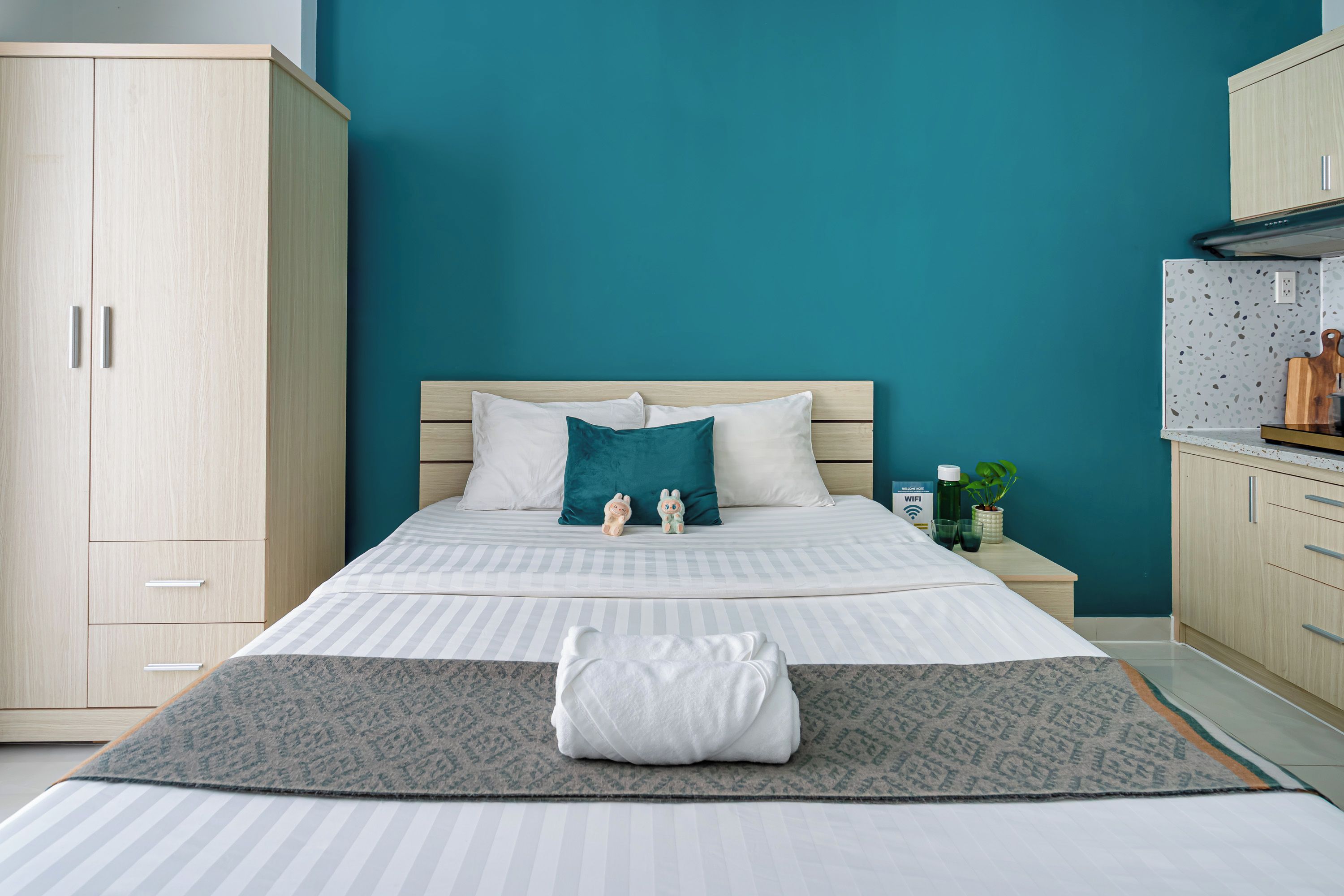 A bedroom with a bed, pillows, a bedside table with a plant, and a wardrobe.