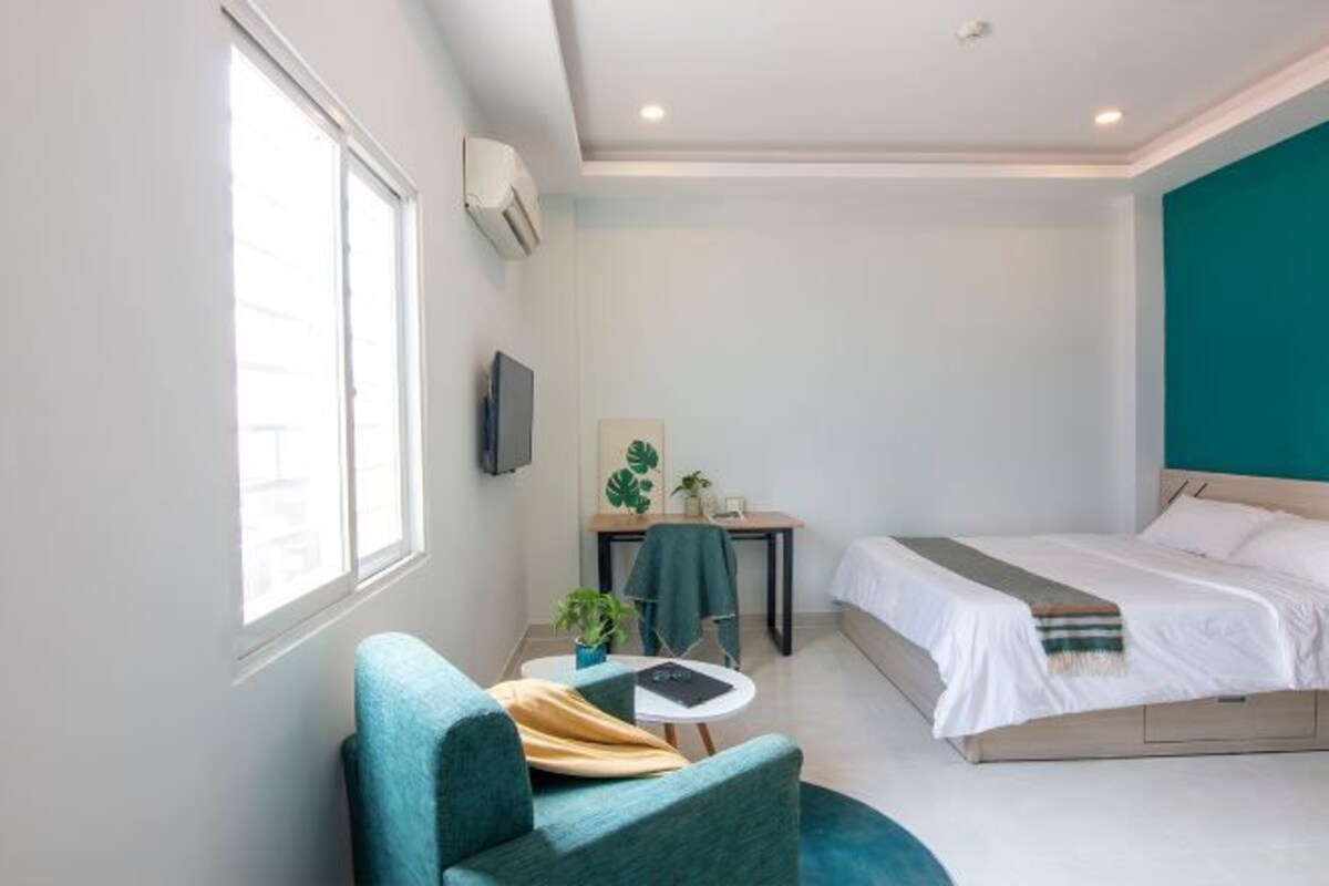 Una habitación de hotel moderna con una cama, un escritorio pequeño, una silla y una ventana.