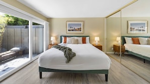 Una camera da letto con un letto grande, due comodini con lampade, uno specchio ampio e una porta scorrevole in vetro che dà su uno spazio all'aperto.
