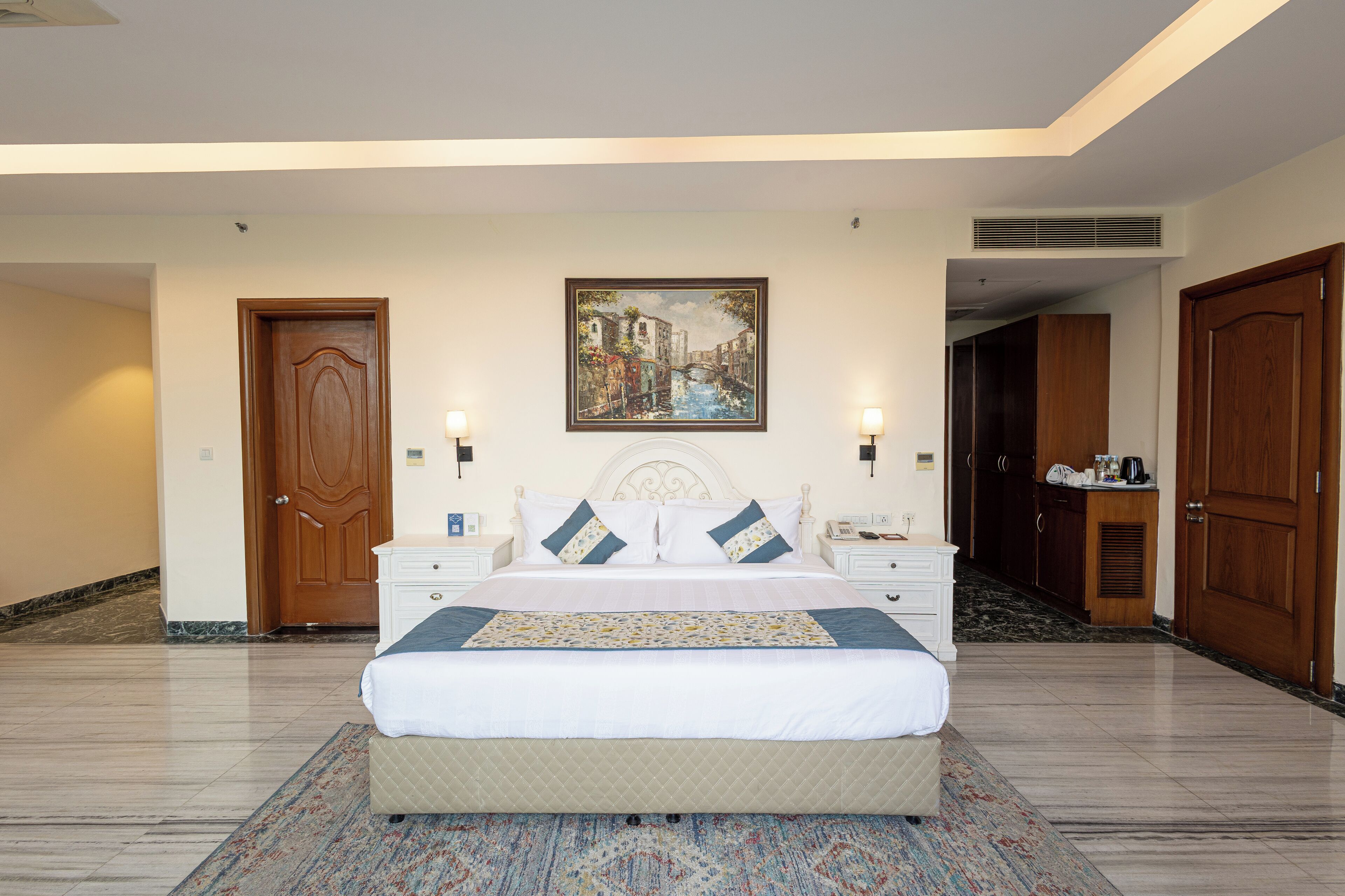 A hotel room with a large bed, a painting on the wall, and a wooden door.