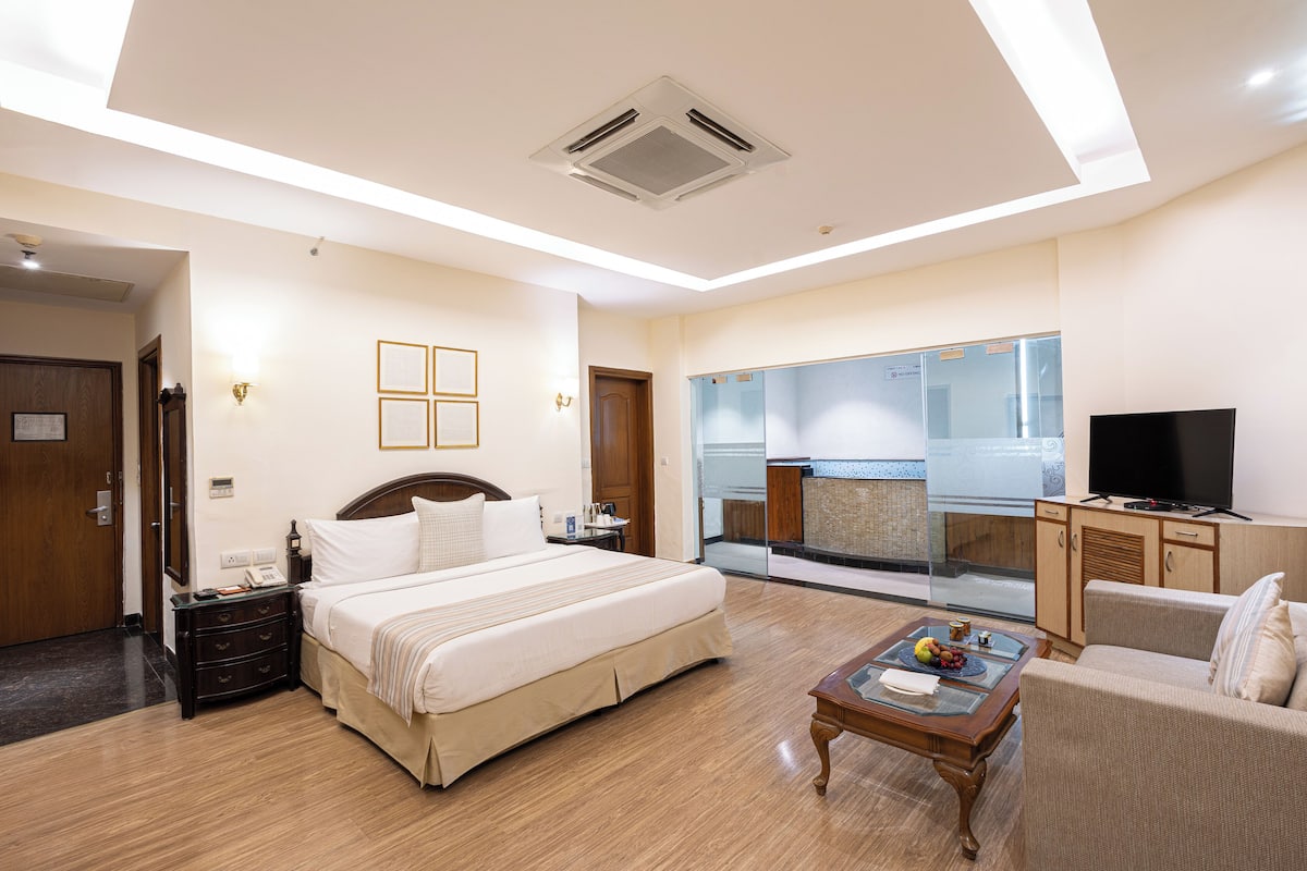 A hotel room with a bed, a desk, a chair, a television, and a minibar.