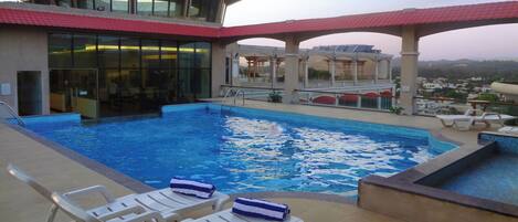A rooftop pool with lounge chairs and a view of the city.