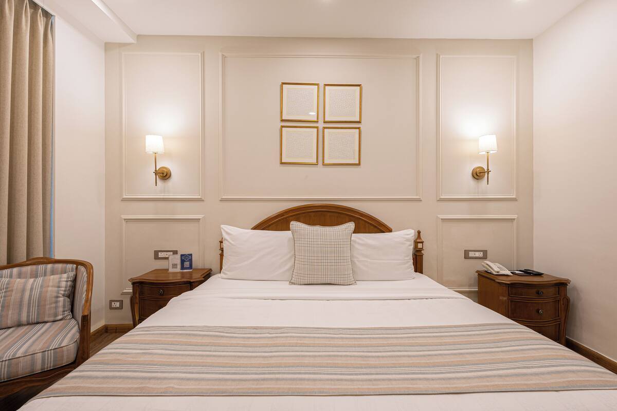 A hotel room with a large bed, two bedside tables, a nightstand, a chair, and a wall-mounted light fixture.