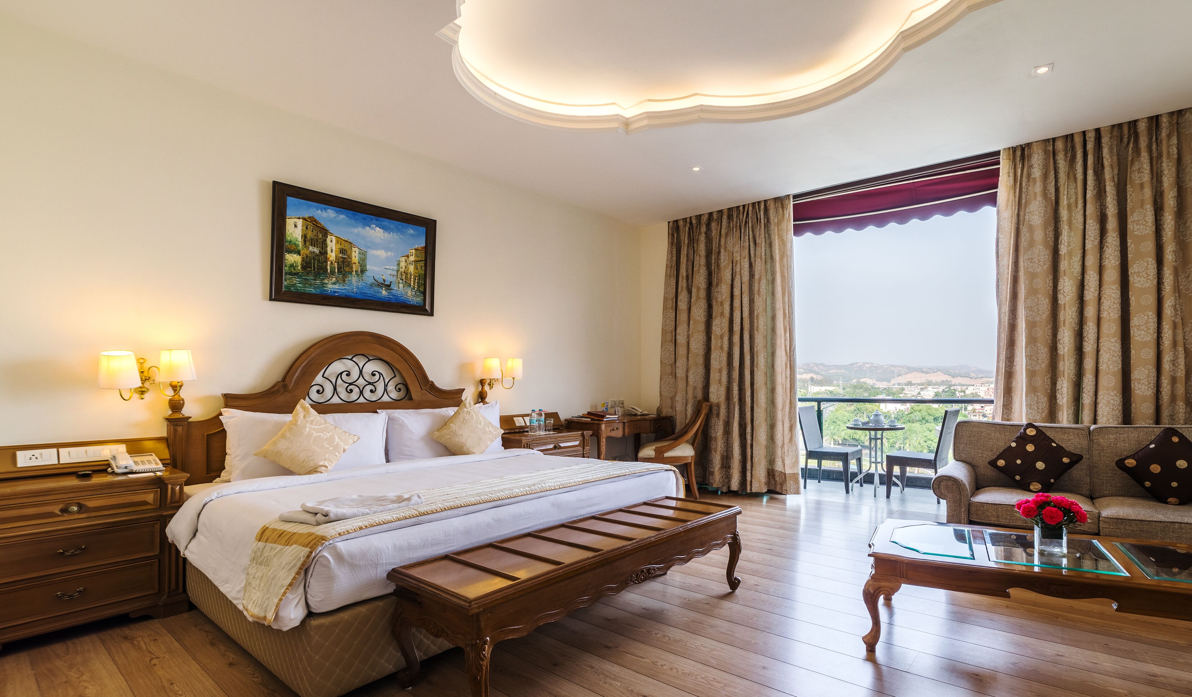A hotel room with a large bed, a desk, a chair, a sofa, and a balcony with a view.
