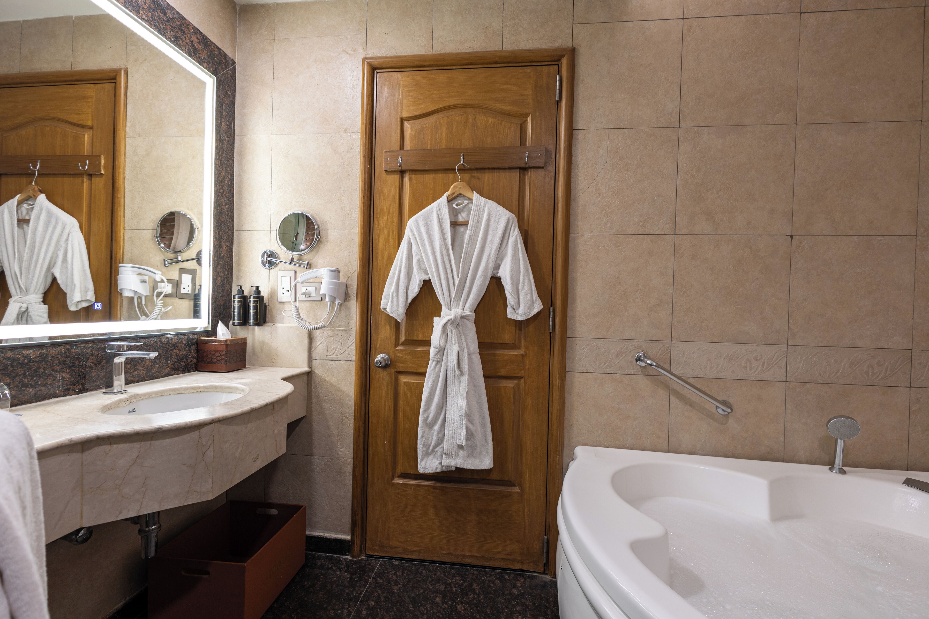 Une salle de bain avec une porte en bois, une baignoire blanche, un lavabo avec un miroir et un porte-serviettes.