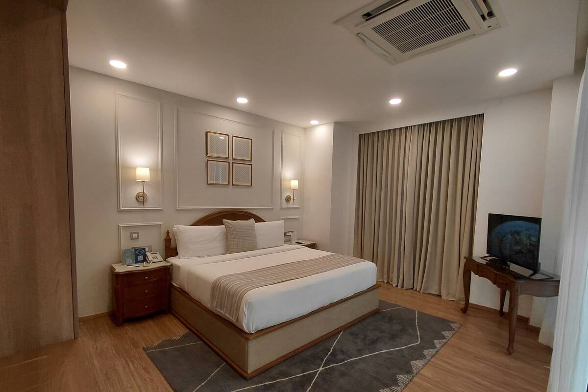 A hotel room with a bed, bedside tables, a TV, and a large window with curtains.