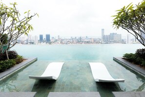 A pool with two white lounge chairs facing a city skyline across a body of water. - Beacon Executive Suites (George Town)