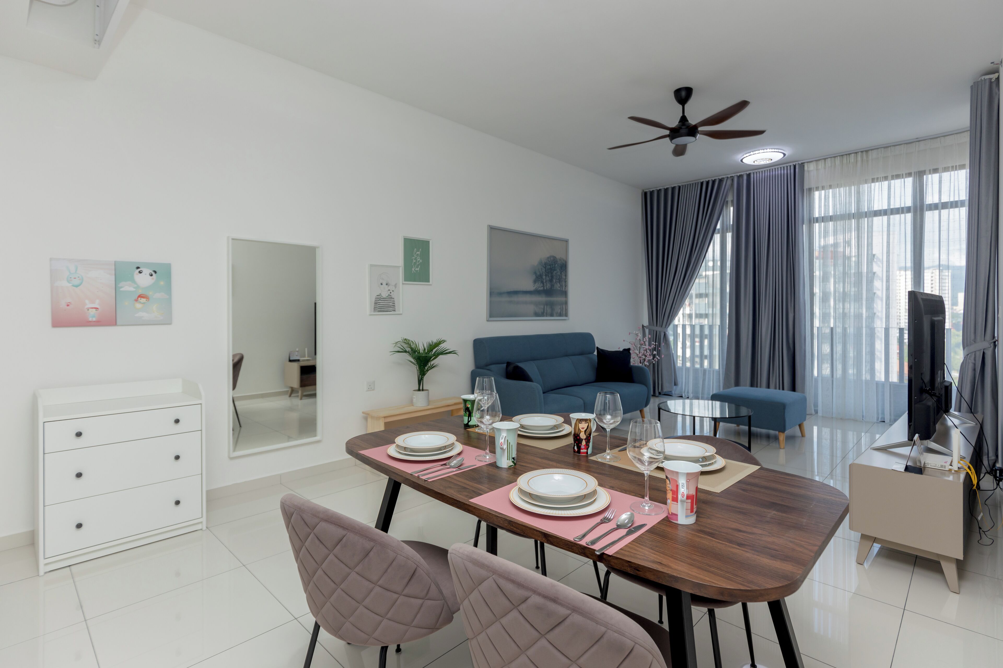 A modern dining area with a wooden table set for four, a blue sofa, a TV, and a ceiling fan.