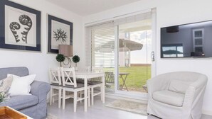 A modern living room with a grey sofa, a white dining table with chairs, a white armchair, and a TV mounted on the wall. - Stylish Ground Floor Apartment with Sea Views (East Wittering)
