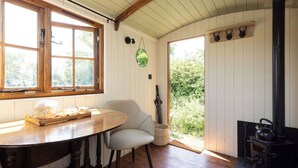 A cozy room with a wooden table, a chair, a window, a door leading outside, and a wood-burning stove. - Harbour Ranch Hut - Rustic Countryside Escape (Emsworth)