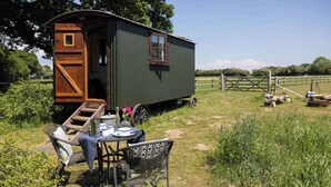 A rustic wooden cabin with a small porch, a table with chairs, and a garden area. - Harbour Ranch Hut - Rustic Countryside Escape (Emsworth)