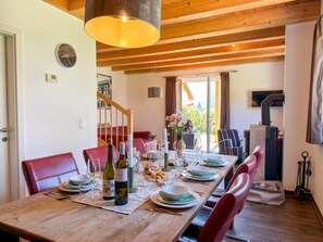 A dining area with a wooden table set for a meal, red chairs, a chandelier, and a view of a garden through a glass door. - Holiday home at ski slopes with mountain views (Kötschach-Mauthen)