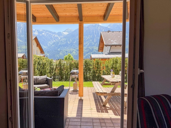A patio with a view of mountains, a grill, and outdoor furniture.