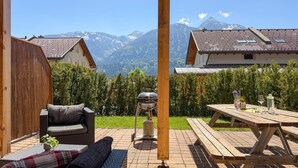 Eine Terrasse mit Grill, einem Holztisch mit Getränken und einer Sitzecke.