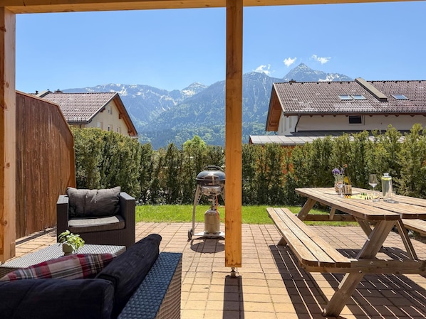 A patio with a grill, a wooden table with drinks, and a sofa. - Holiday home at ski slopes with mountain views (Kötschach-Mauthen)
