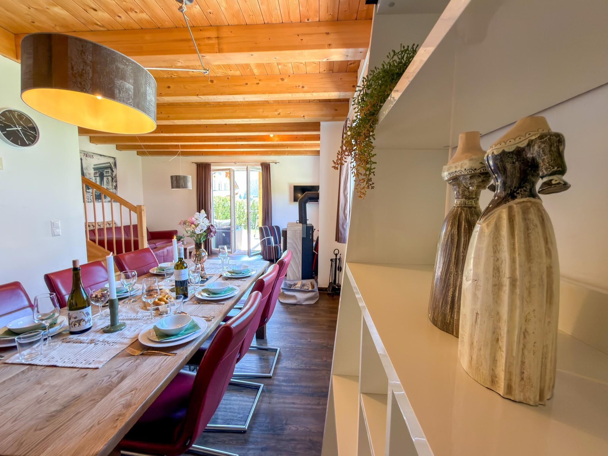 Un coin repas avec une table en bois dressée pour le repas, des chaises rouges et un luminaire suspendu.