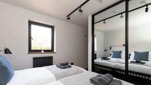 A modern hotel room with two beds, a large mirror, a window, and a radiator.