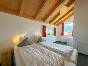 Un dormitorio con dos camas, vigas de madera en el techo, una ventana con cortinas rojas y vistas a la montaña.