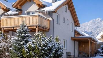 Ein zweistöckiges Chalet mit Balkon, Holzfassade und verschneiter Umgebung.