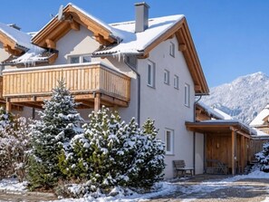 A two-story chalet with a balcony, wooden exterior, and snow-covered surroundings.