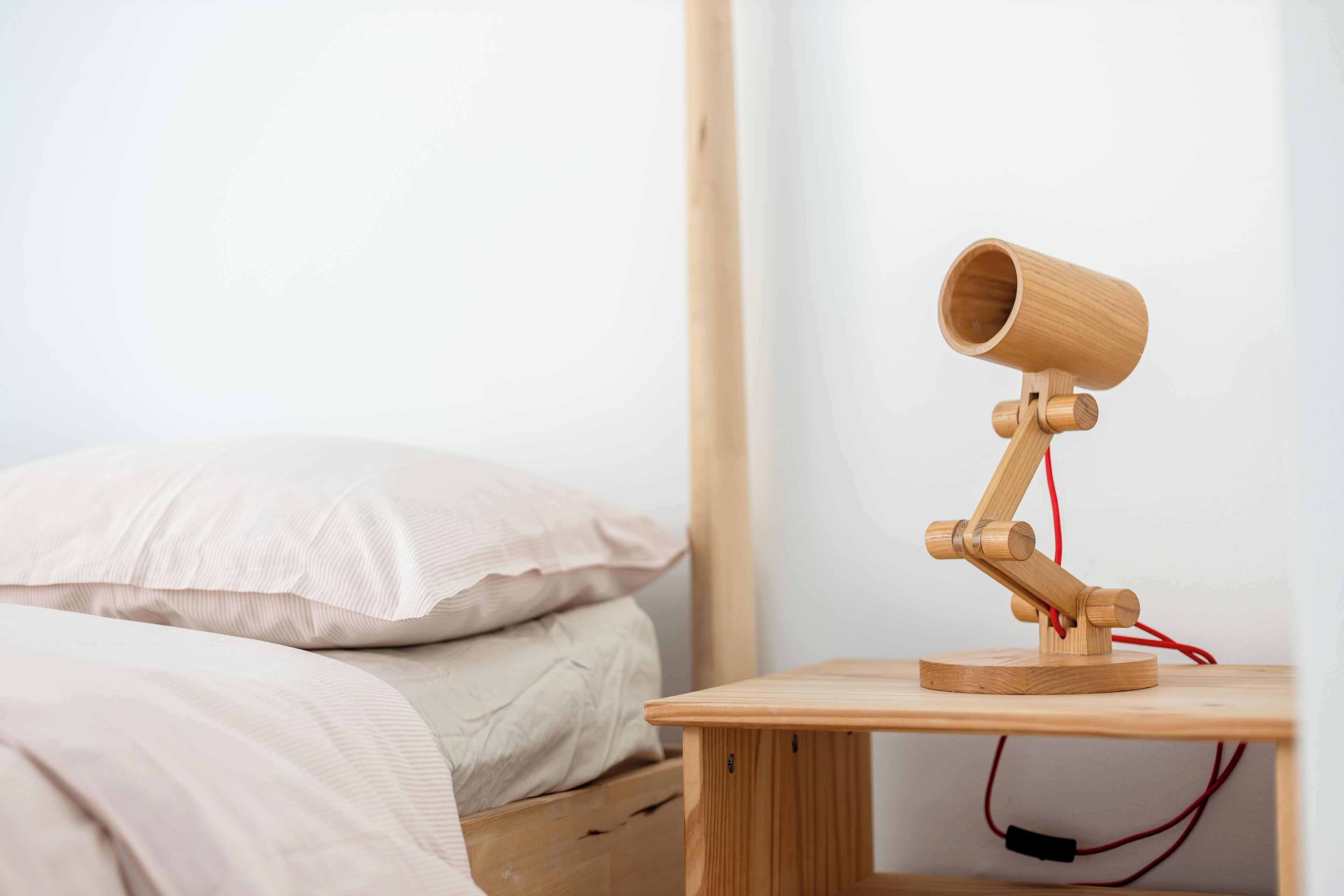A wooden desk with a camera on it, a bed with pillows, and a white wall.