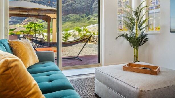 A living room with a sofa, a small table, and a view of a mountainous landscape through large windows.