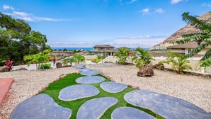 A pathway with stepping stones leading to a house with a view of the ocean.