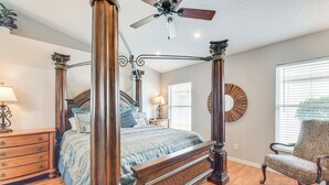 Un lit à baldaquin avec un ventilateur de plafond, une commode en bois, une chaise et un miroir rond accroché au mur.