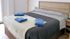 Ein ordentlich bezogenes Bett mit Holzkopfseitenverkleidung, ein Nachttisch mit Lampe und ein Kleiderständer an einer weißen Wand.