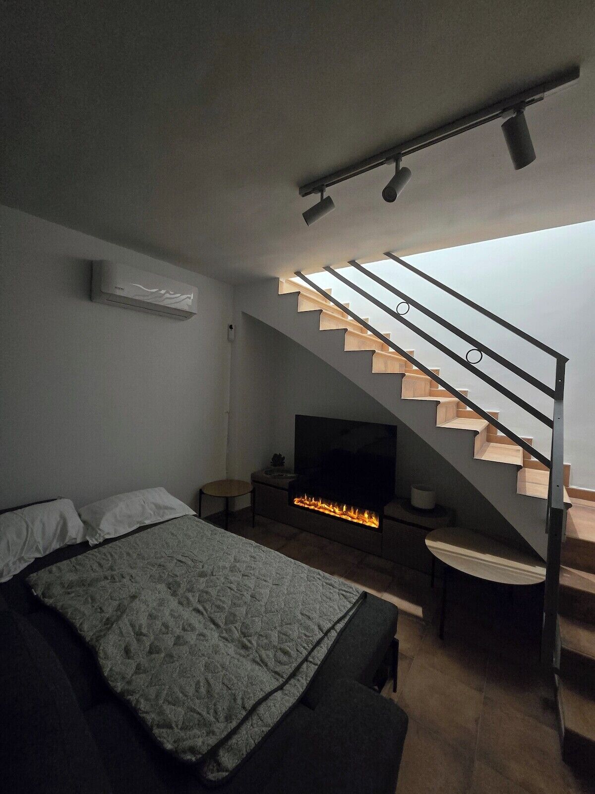 Ein modernes Schlafzimmer mit einem Bett, einem Fernseher, einem Kamin und einer Treppe.