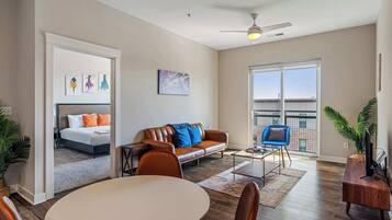 A spacious living room with a dining area, a sofa, a TV stand, and a balcony with a view.
