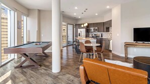 A modern living space with a pool table, dining area, kitchen, and large windows. - CozySuites - Penrose (Indianapolis)