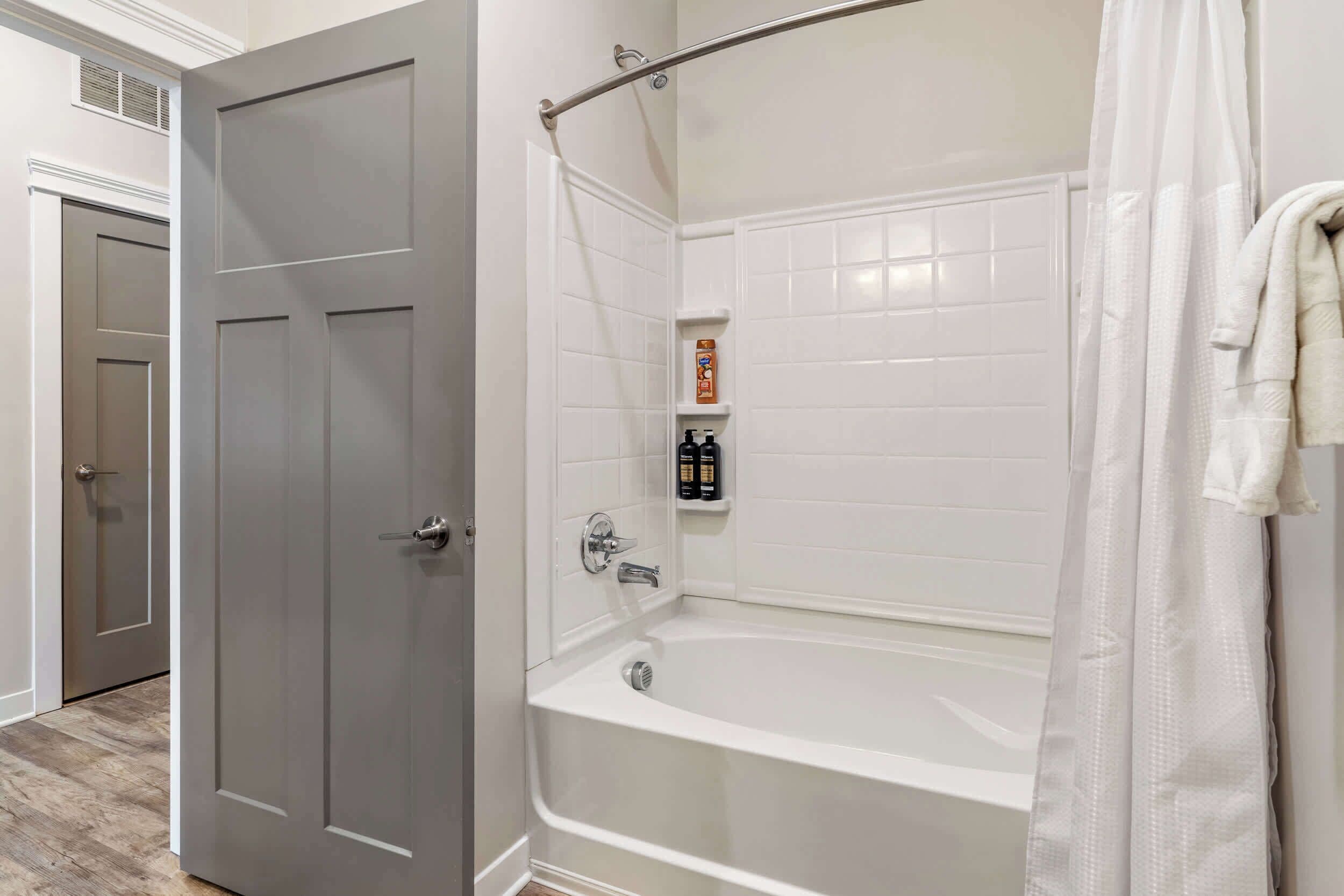 Un bagno con vasca, doccia e una porta. Prodotti da bagno su uno scaffale.
