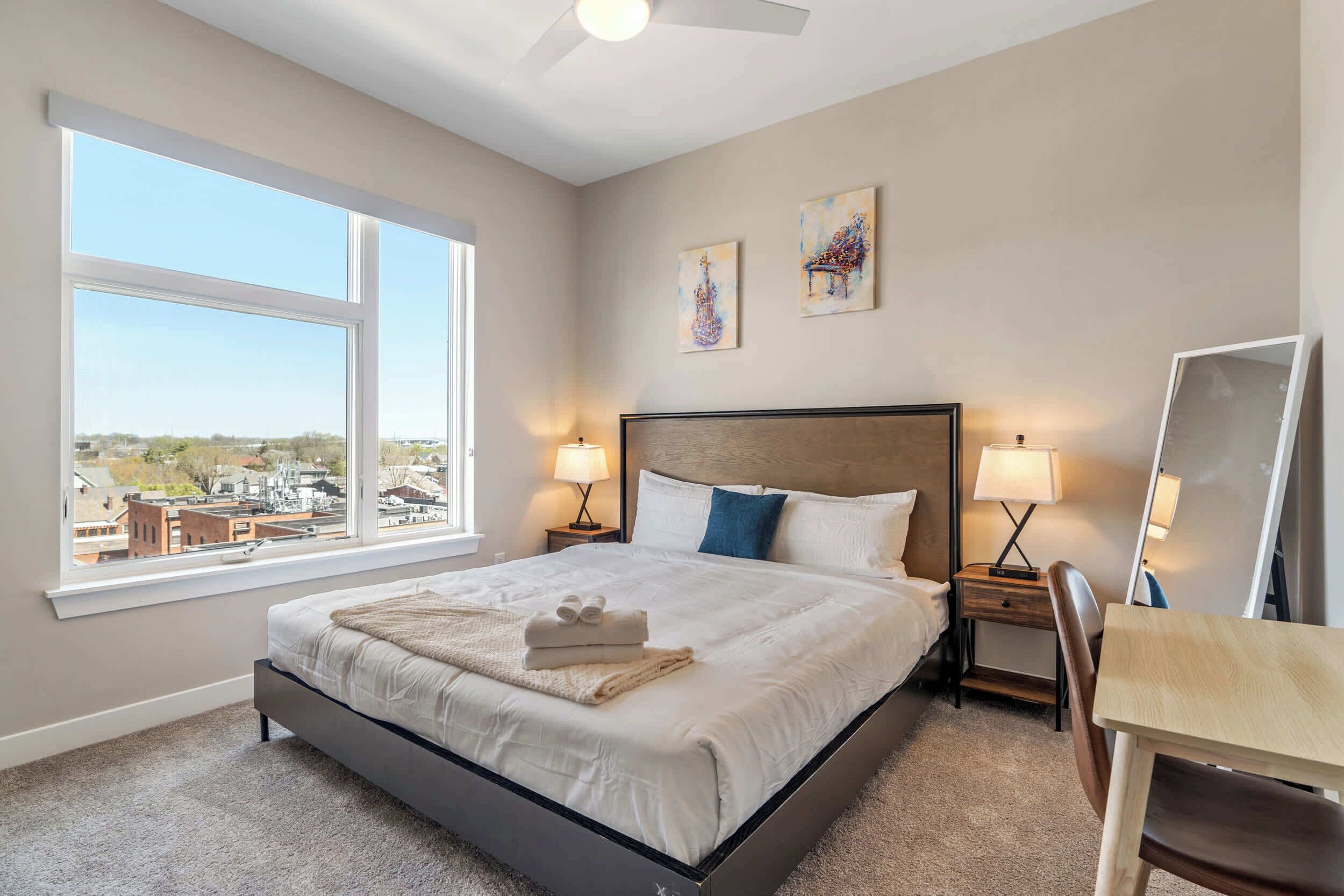 A hotel room with a large bed, two bedside lamps, a desk, and a chair.