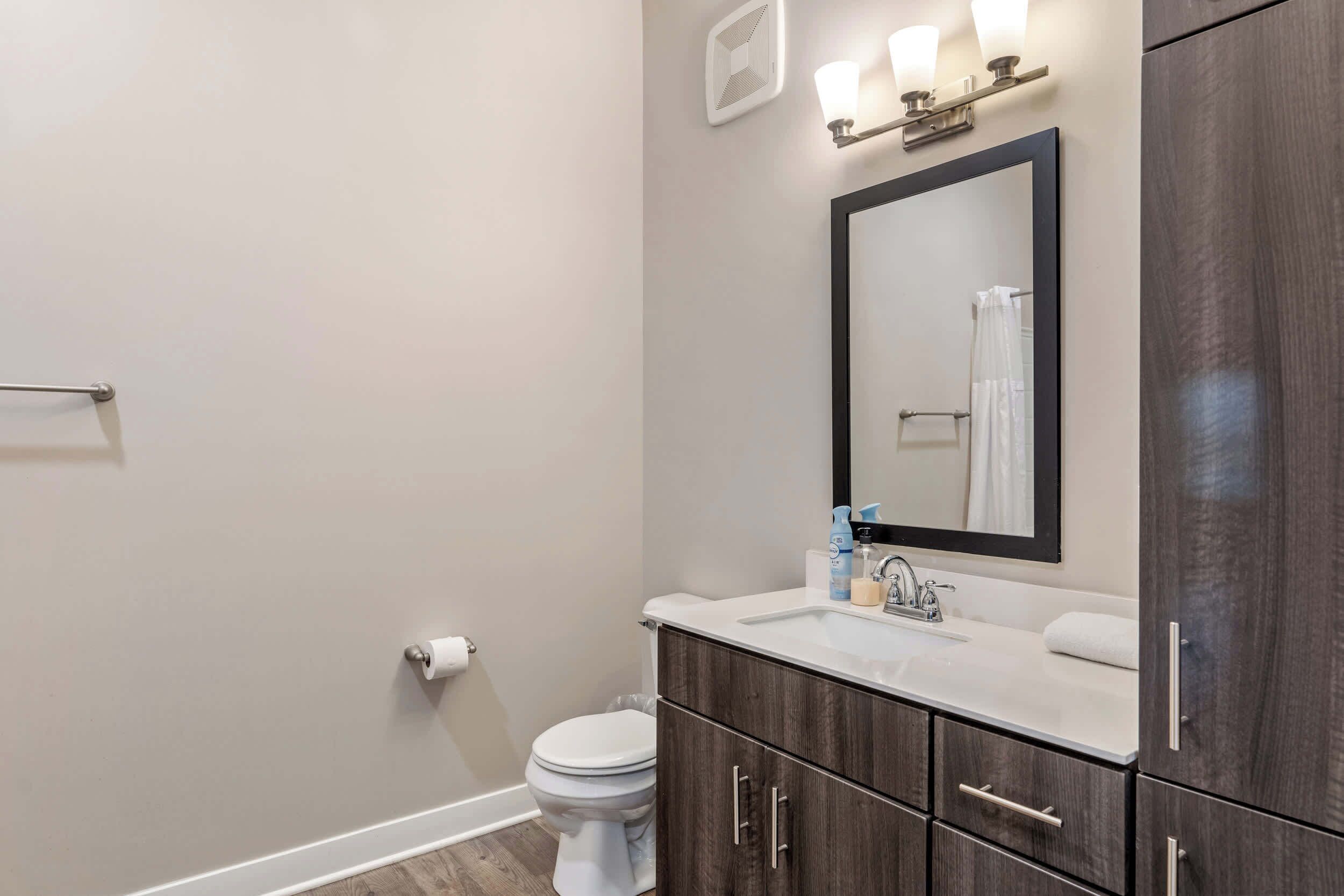 A modern bathroom with a white toilet, dark wood cabinets, a white sink, and a mirror above it.