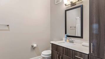 A modern bathroom with a white toilet, dark wood cabinets, a white sink, and a mirror above it.
