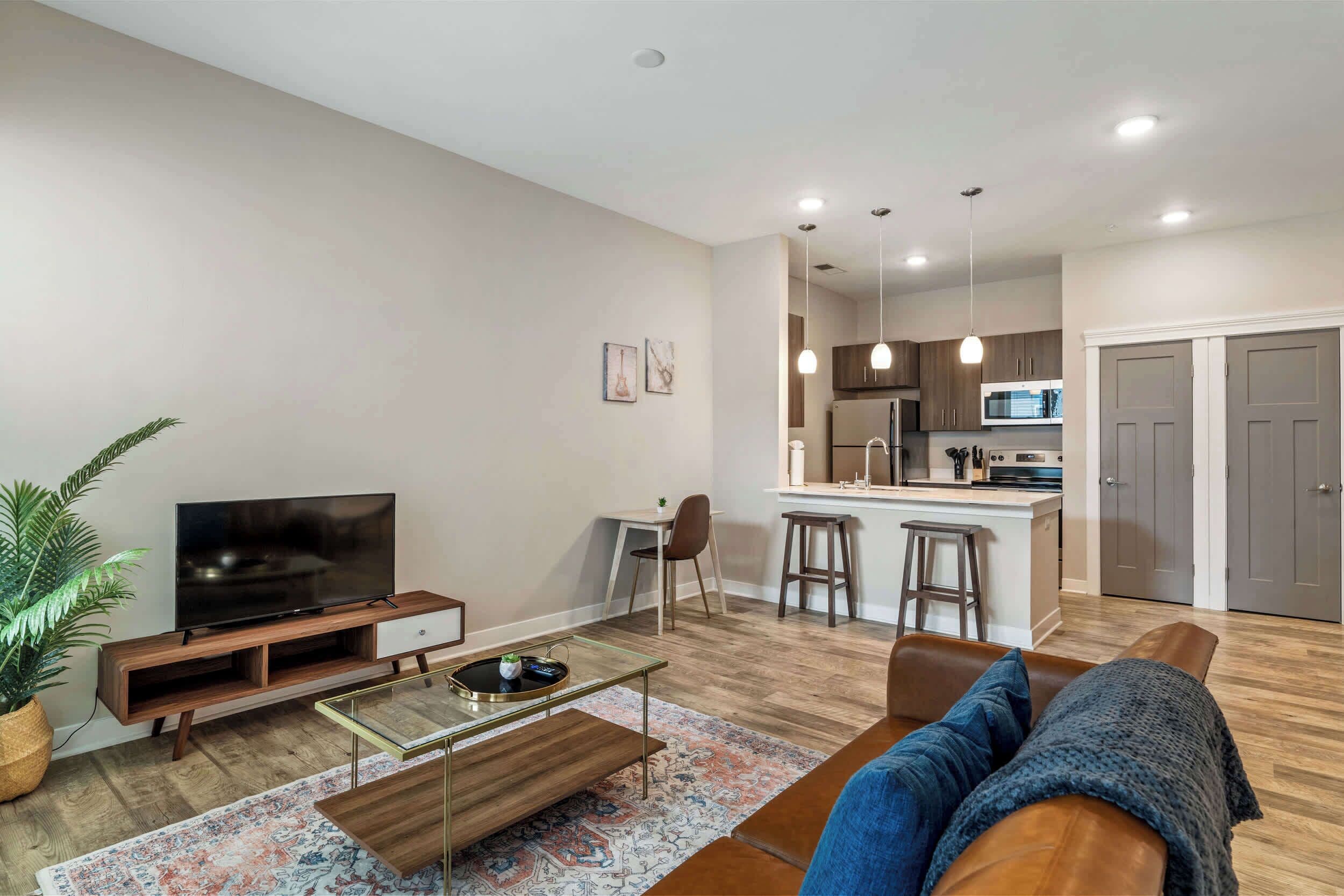 A modern living room with a TV, coffee table, sofa, and a kitchen in the background.