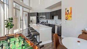 A modern kitchen with a central island, bar stools, and a foosball table. - CozySuites - Penrose (Indianapolis)