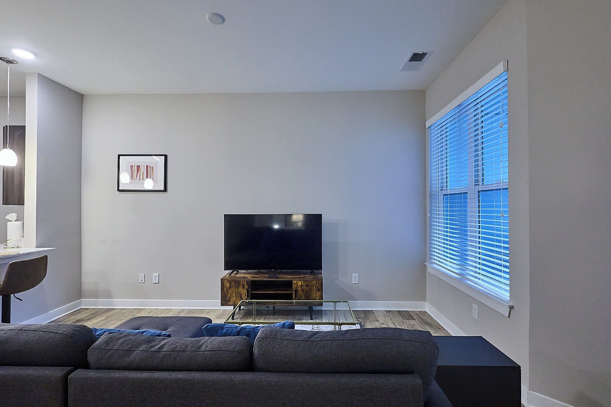 A modern living room with a flat-screen TV on a wooden stand, a glass coffee table, and a gray sofa.